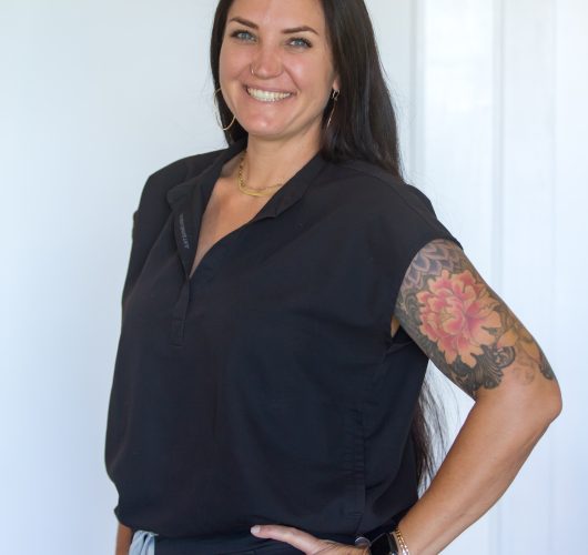 Paradise Medical Maui, Smiling healthcare worker in black scrubs with floral tattoo on arm.